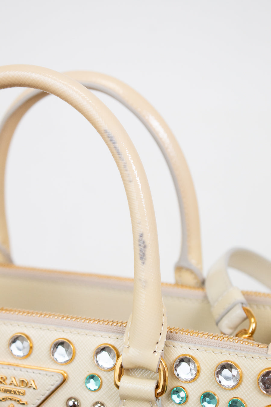 Close-up of strap on beige handbag with decorative stones on a light gray background showing stain on handle 