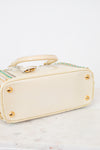 Bottom exterior  of cream-colored handbag with gold accents on a white background