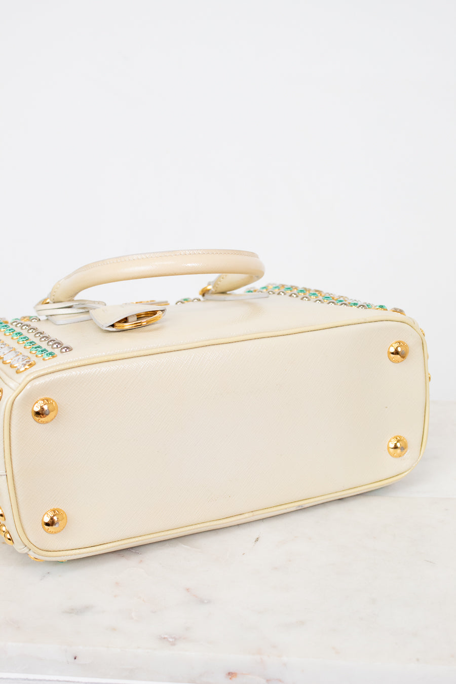 Bottom exterior  of cream-colored handbag with gold accents on a white background