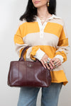 Person wearing a yellow and beige striped shirt holding a maroon Prada handbag against a white background