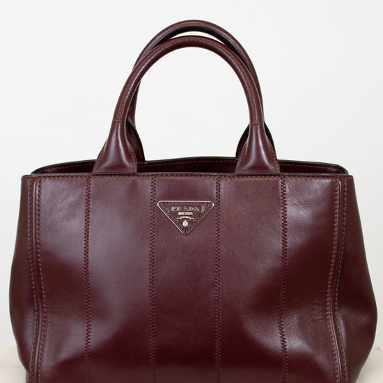 Maroon leather handbag with a visible brand logo on a light wooden surface.