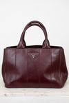 Maroon leather handbag with a visible brand logo on a light wooden surface.