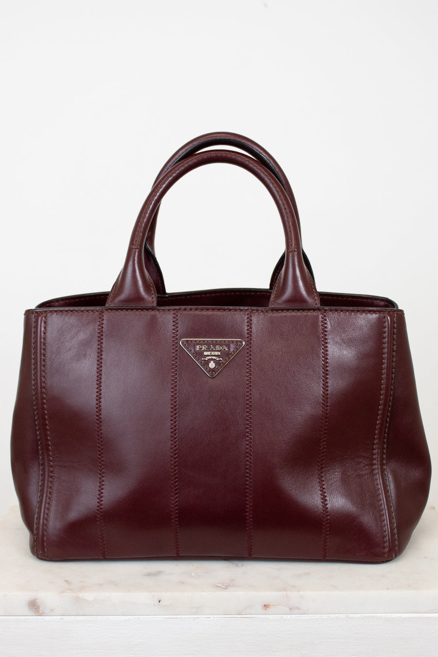 Maroon leather handbag with a visible brand logo on a light wooden surface.
