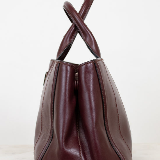 Maroon leather handbag with a cross-shaped handle on a white background