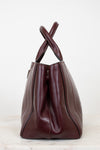 Maroon leather handbag with a cross-shaped handle on a white background