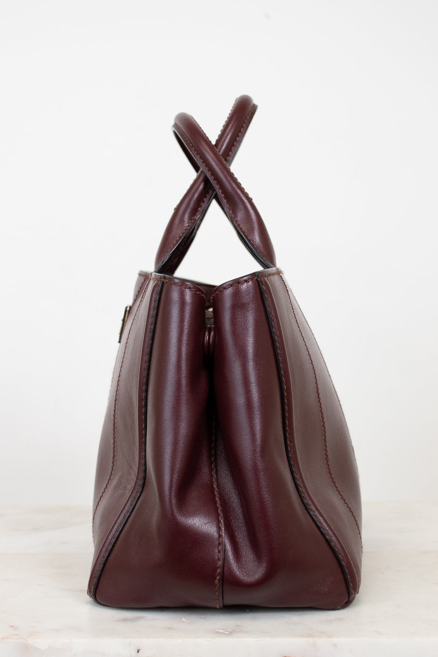 Maroon leather handbag with a cross-shaped handle on a white background