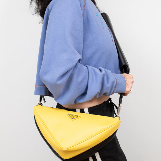Person wearing a blue sweatshirt and black pants with a yellow Prada handbag on a white background