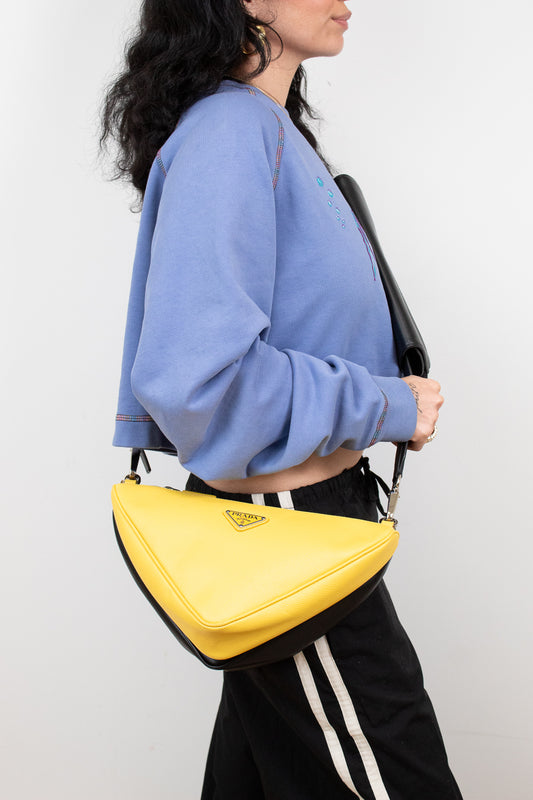 Person wearing a blue sweatshirt and black pants with a yellow Prada handbag on a white background