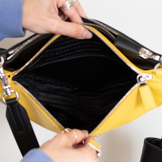 Person opening a yellow handbag with black interior on a white background