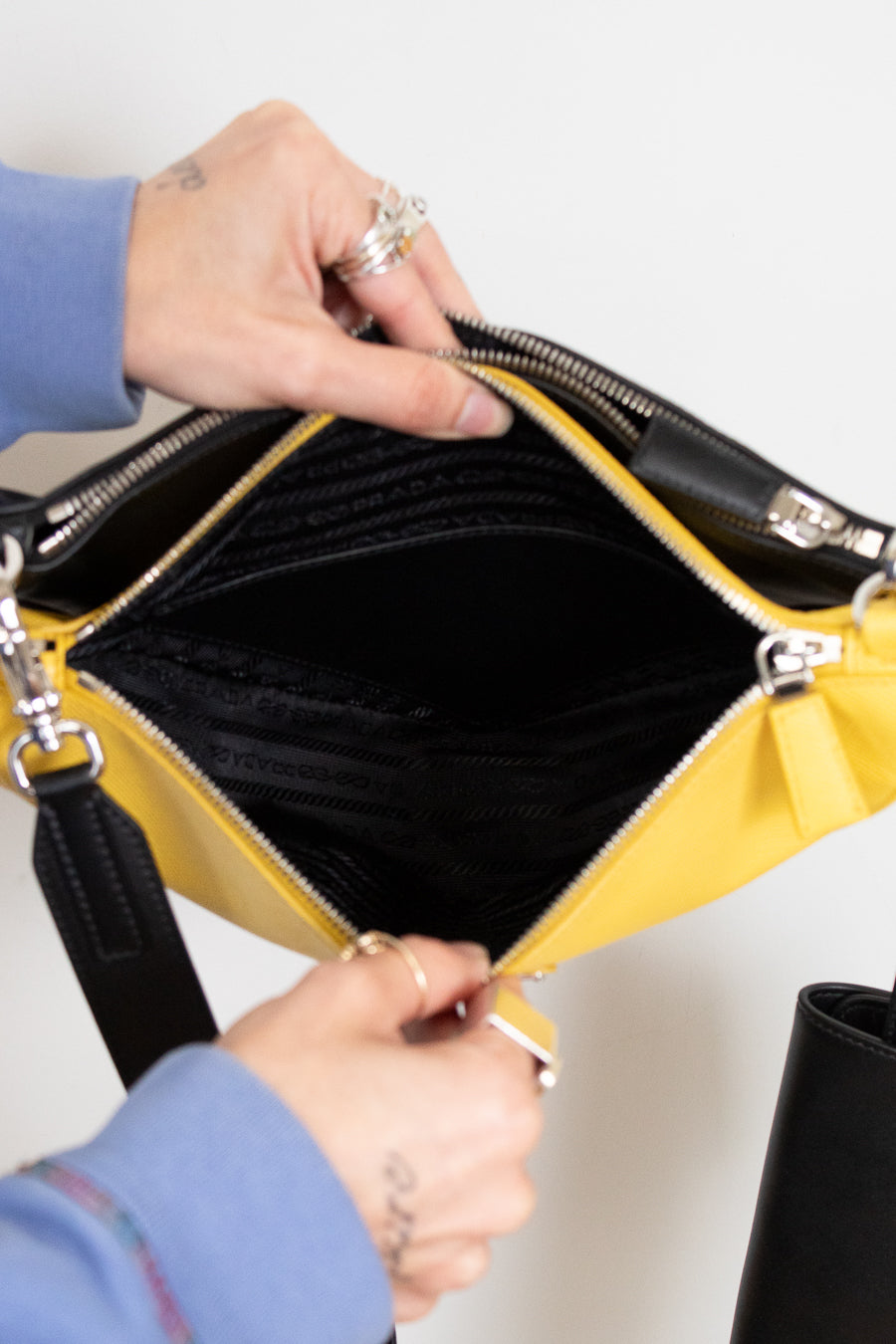 Person opening a yellow handbag with black interior on a white background