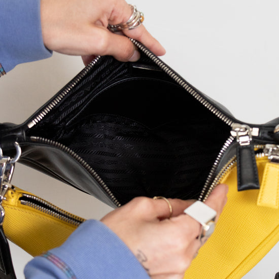 Person opening a black handbag with a yellow pouch on a light gray background