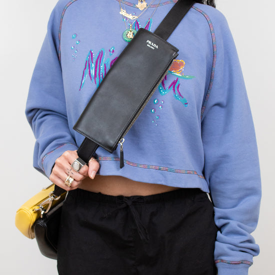 Person wearing a blue sweatshirt with colorful graphics and text, holding a black crossbody bag.