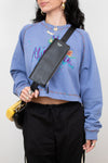 Person wearing a blue sweatshirt with colorful graphics and text, holding a black crossbody bag.