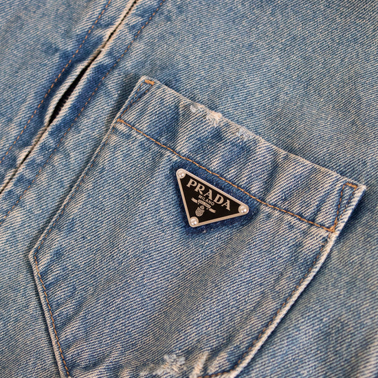 Close-up of a blue denim jacket with a Prada logo on the pocket.