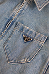 Close-up of a blue denim jacket with a Prada logo on the pocket.