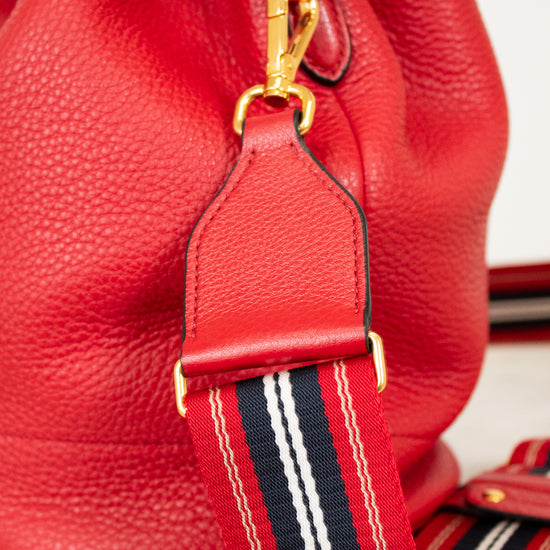 Red leather bucket bag with a striped strap on a light background