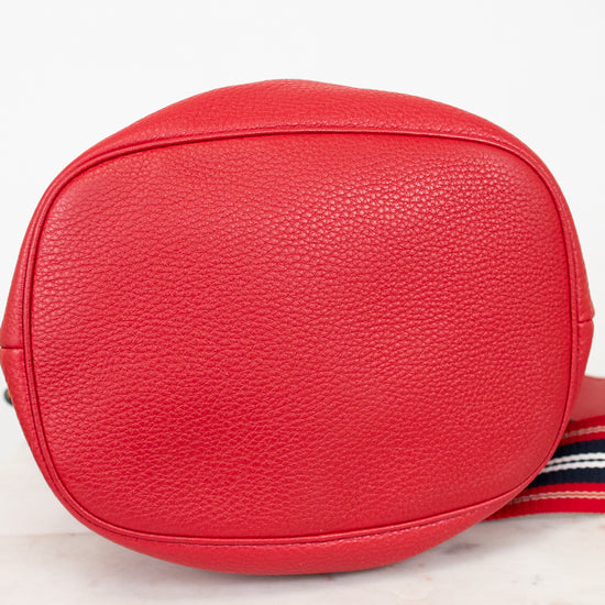 Red textured crossbody bag with a striped strap on a light background