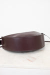 A dark burgundy leather shoulder bag with a wide, structured strap, resting on a white marble surface against a white background.