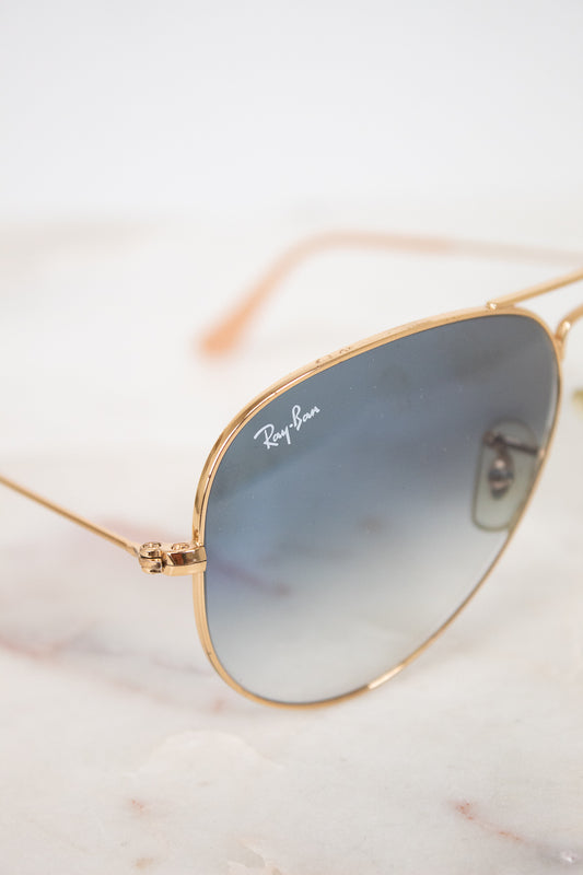 Gold-framed sunglasses with gradient lenses on a marble surface