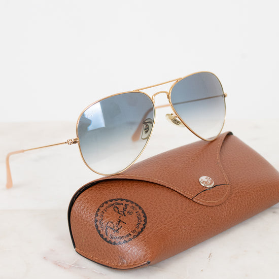 Aviator sunglasses with gold frame and blue-tinted lenses on a brown leather case.