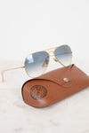Aviator sunglasses with gold frame and blue-tinted lenses on a brown leather case.