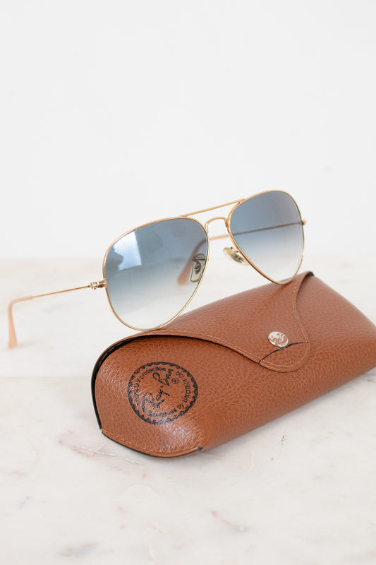 Aviator sunglasses with gold frame and blue-tinted lenses on a brown leather case.