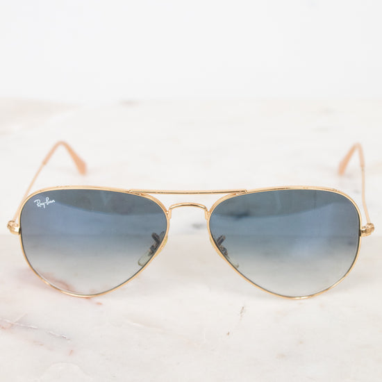 Gold-framed sunglasses with blue gradient lenses on a white marble surface