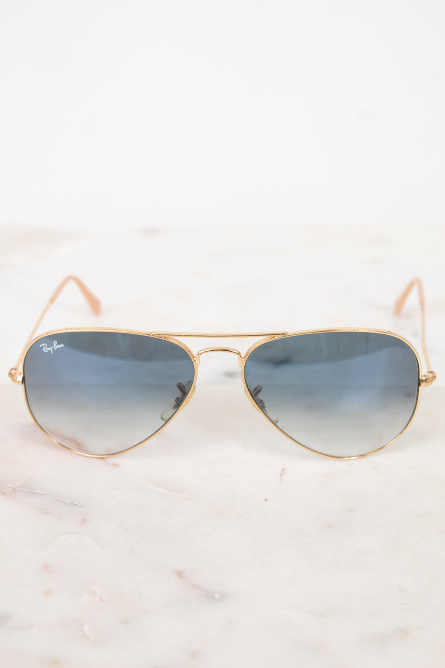 Gold-framed sunglasses with blue gradient lenses on a white marble surface