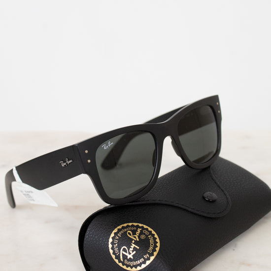 Black sunglasses with white accents on a black case with a gold logo, on a light marble surface.