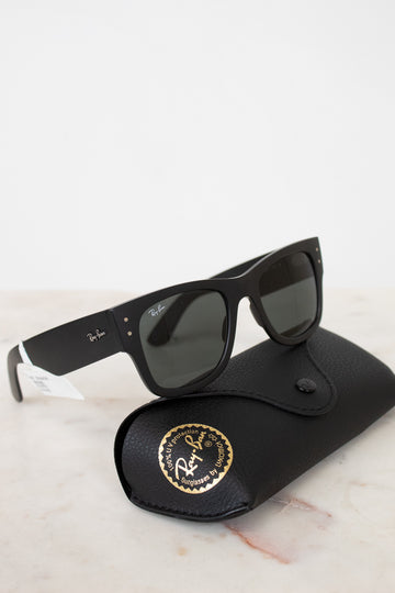 Black sunglasses with white accents on a black case with a gold logo, on a light marble surface.