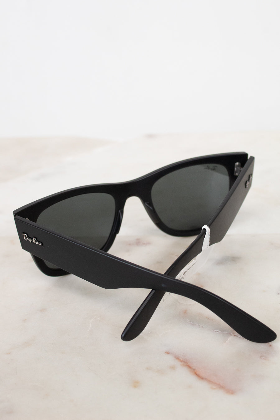 Black sunglasses with a Ray-Ban logo on a light marble background