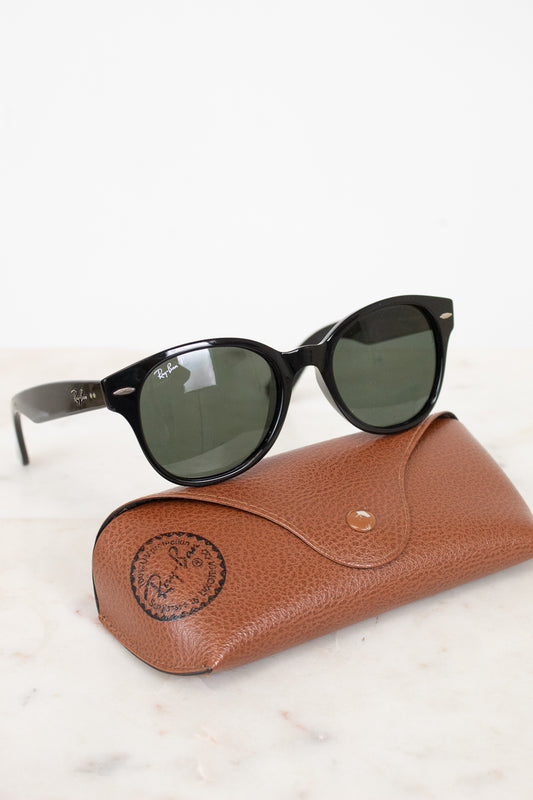 Black sunglasses with black lenses on a brown leather case against a white background