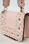 Pink handbag with floral patterns and gold studs on a light background