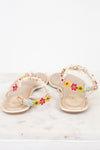 A pair of beige flat sandals decorated with colorful flowers and white lace detail on straps, displayed on a light marble surface against a white background.