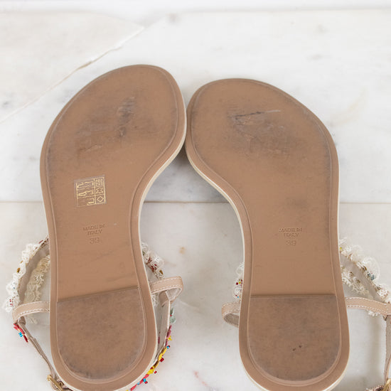 A pair of women's flat sandals shown from the bottom sole, resting on a white marble surface. 