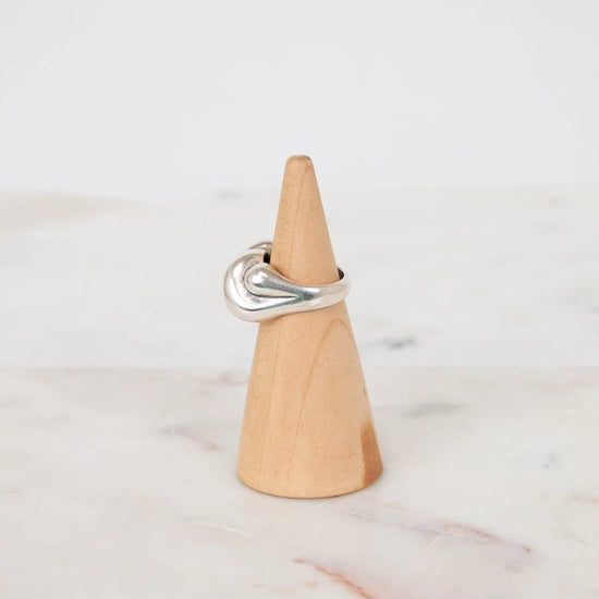Silver ring on a wooden cone against a white background