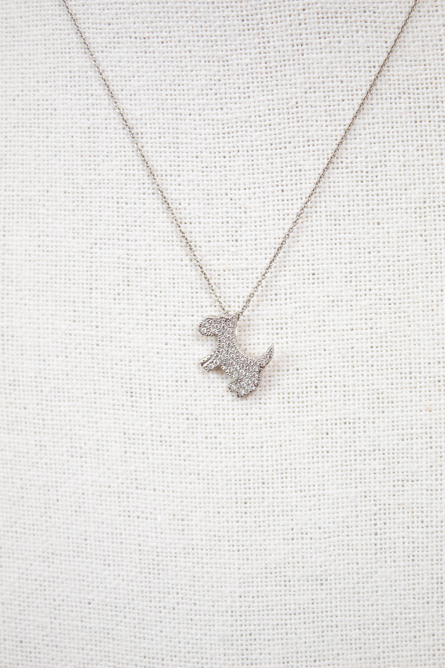 Silver necklace with a dog-shaped pendant on a light gray textured background