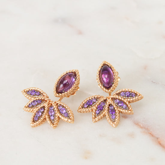 Gold earrings with purple gemstones on a marble surface