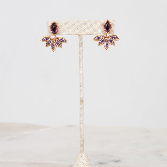 Purple and gold earrings on earring stand with white background