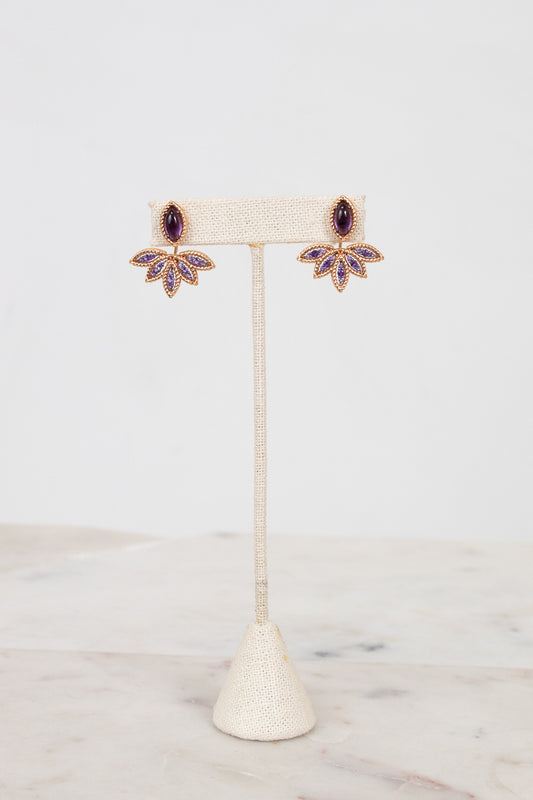 Purple and gold earrings on earring stand with white background