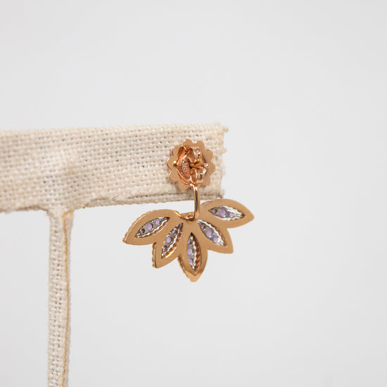 Gold leaf-shaped earring on a beige ribbon against a light gray background