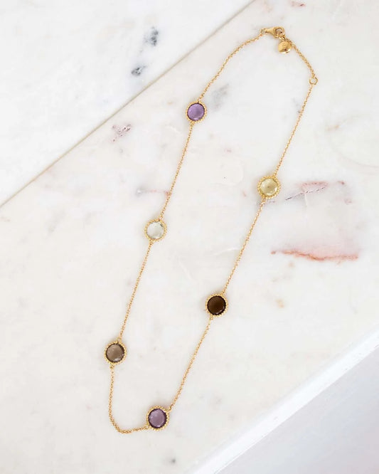Gold necklace with various colored stones on a marble surface