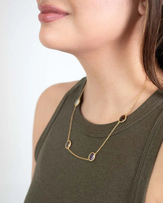 Woman wearing a gold necklace with gemstones on a plain background