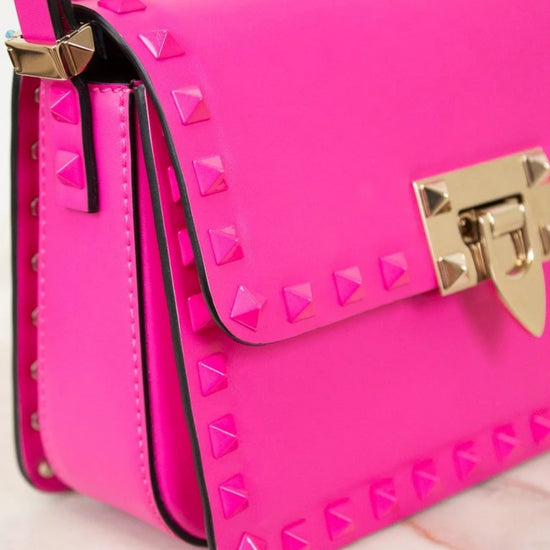 Pink studded handbag with gold accents on a light pink background