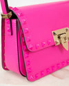 Pink studded handbag with gold accents on a light pink background