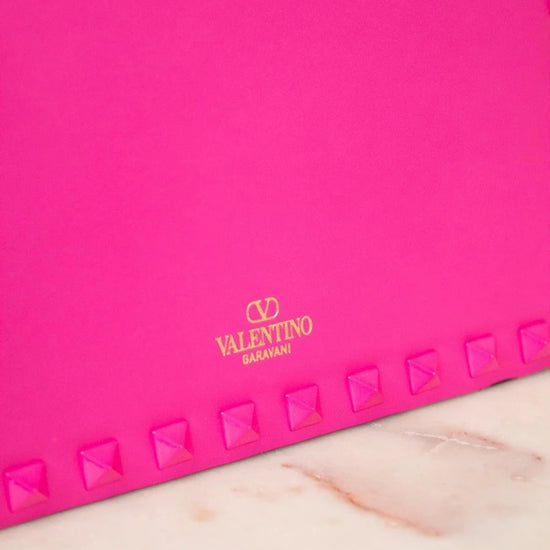 Pink clutch with studded details and Valentino logo on a marble surface
