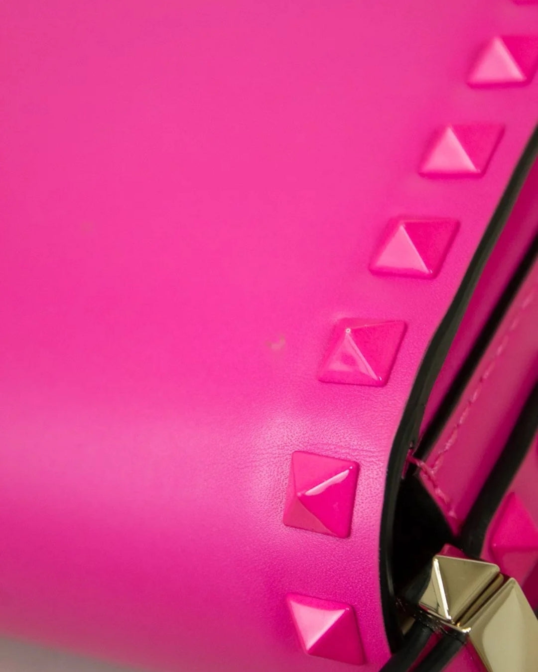 Close-up of a pink handbag with pyramid studs and a gold clasp.