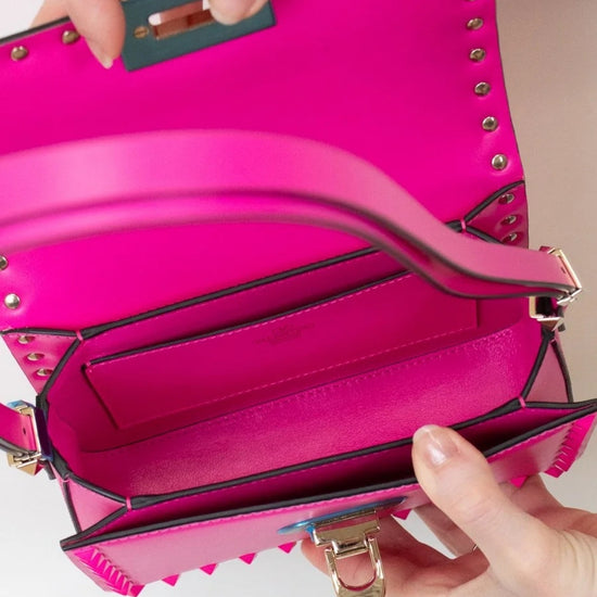 Pink handbag with gold studs held by a person's hands on a light background