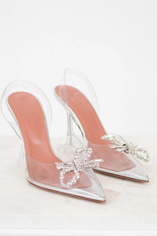 Clear high-heeled shoes with pink soles and decorative bows on a white background