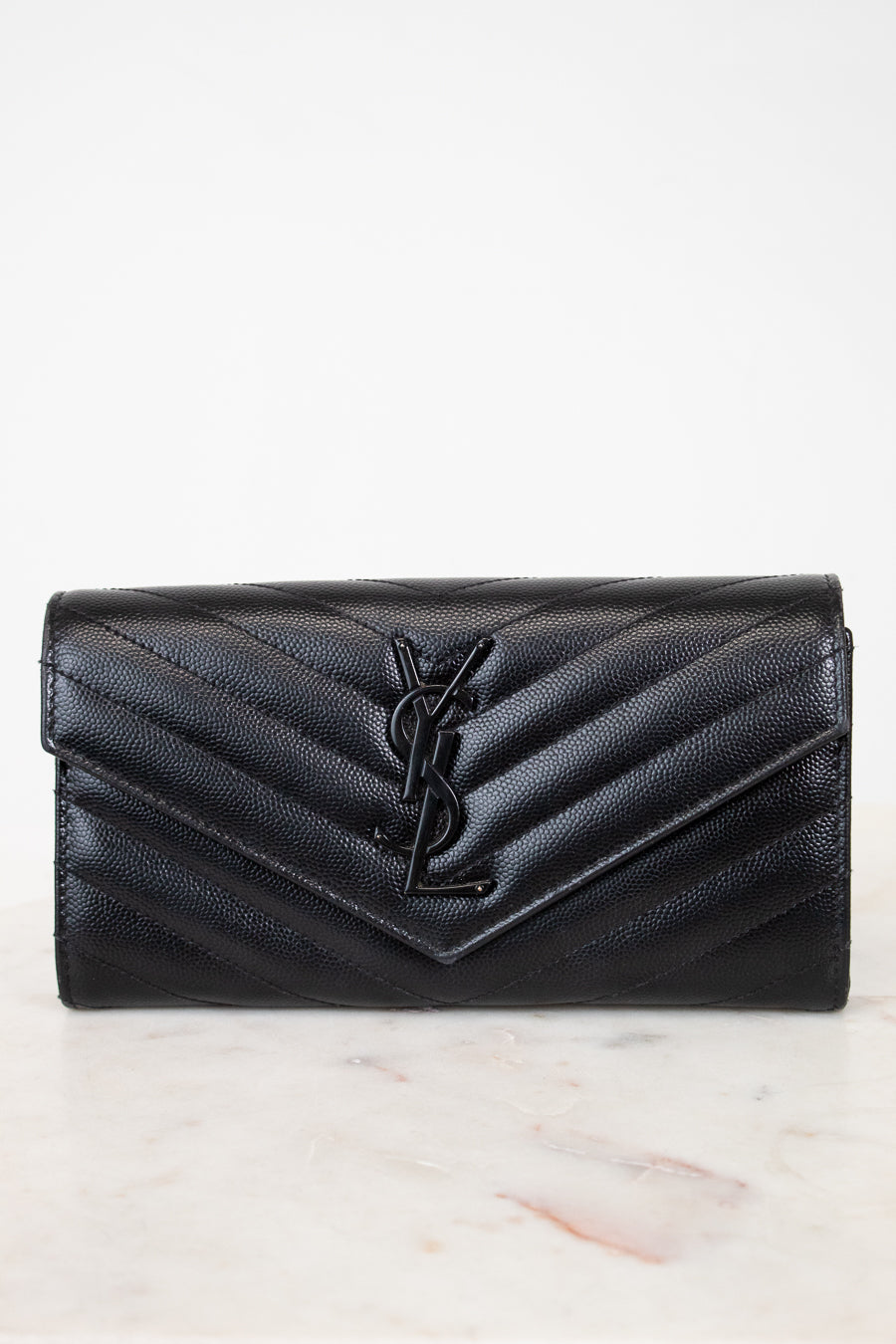 Black quilted wallet with a brand logo on a light marble background